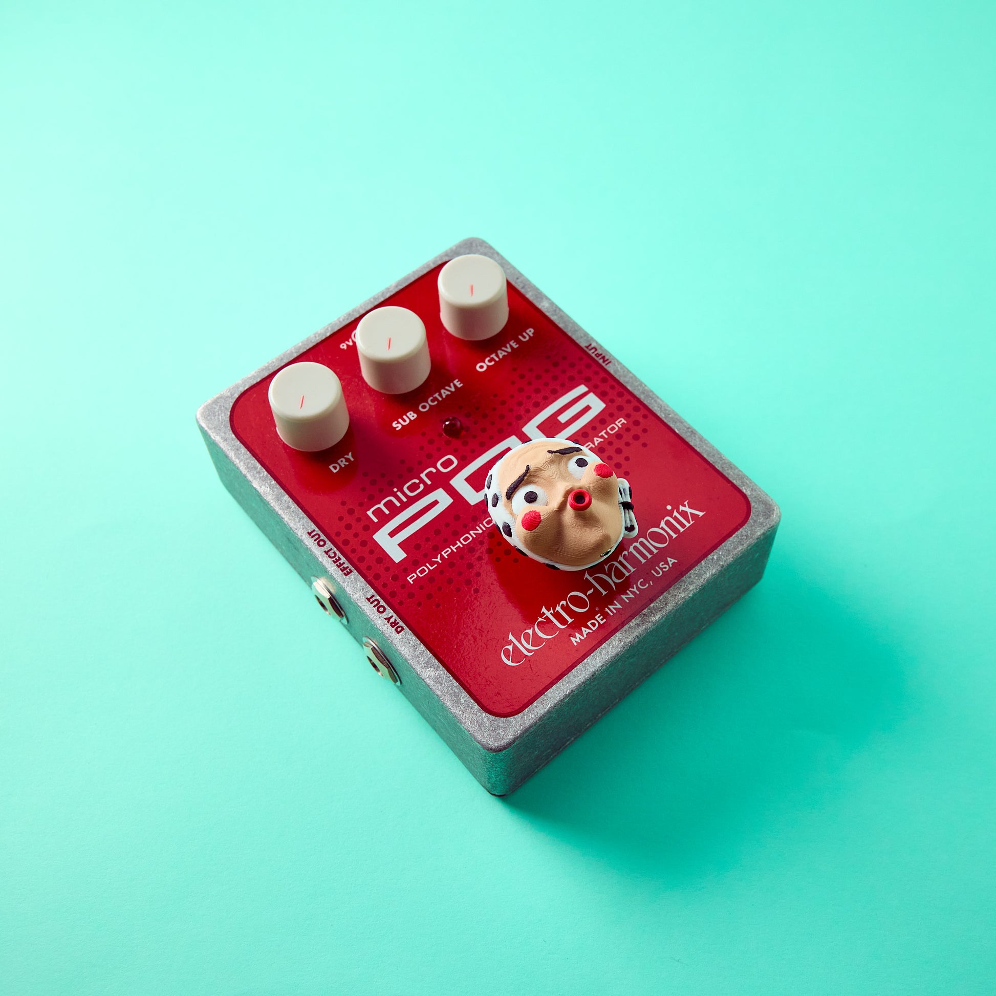 Hyottoko Topper — Japanese folk mask topper installed on red effects pedal top angle view for guitar and bass