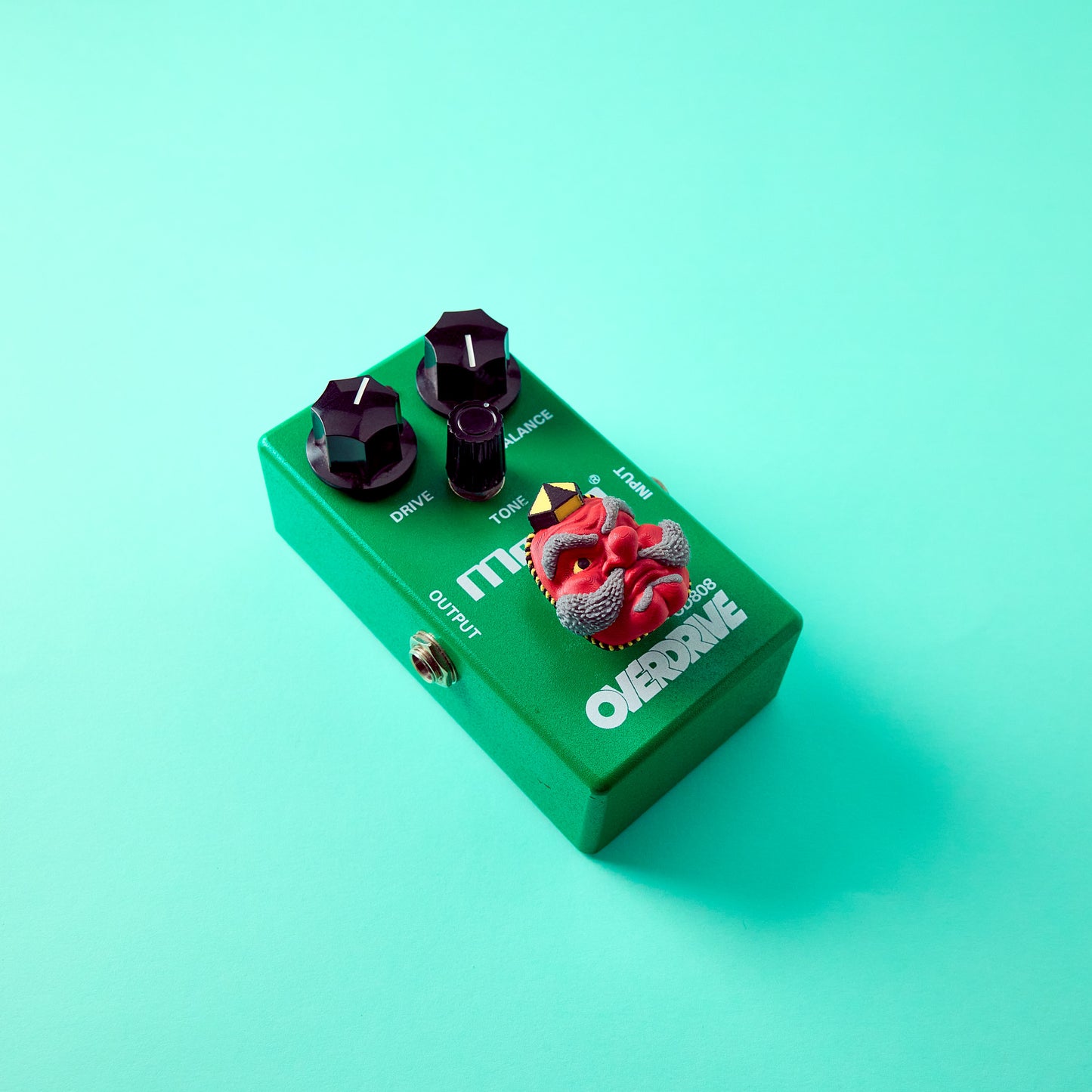 Tengu Topper — Japanese demon mask topper installed on Ibanez Tube Screamer green effects pedal top angle view for guitar and bass